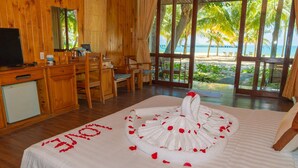A room with a bed adorned with rose petals and the word "LOVE" spelled out, a wooden desk with a television, and a view of the beach through large windows. - Tan Son Nhat Con Dao Resort (Ho Chi Minh City)