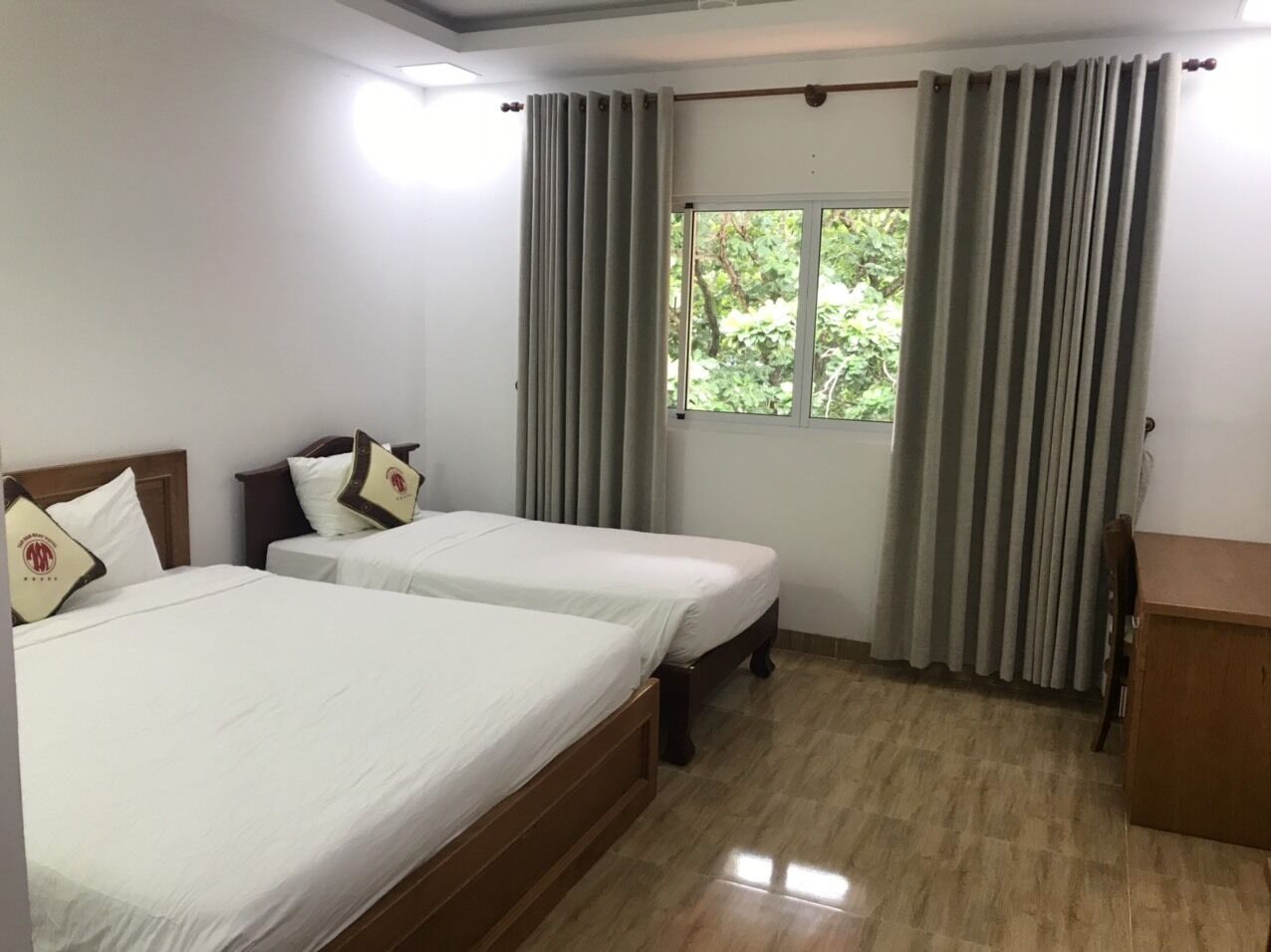 Ein Hotelzimmer mit zwei Einzelbetten, einem Holzkopfstück, einem kleinen Schreibtisch aus Holz und einem Fenster mit Vorhängen.