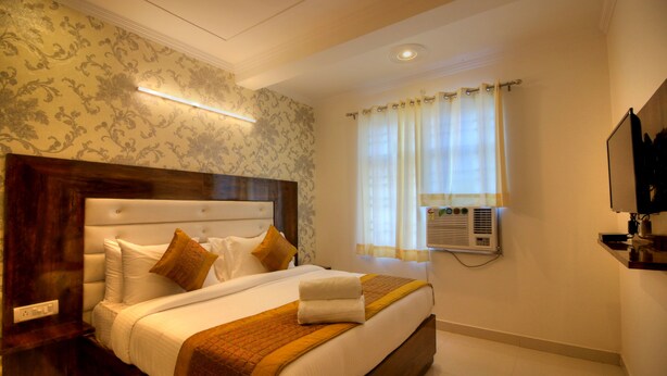 Habitación de hotel con una cama grande, cabecera de madera, aire acondicionado de pared y televisión en la pared.
