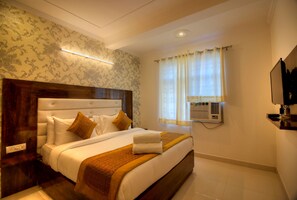 Ein Hotelzimmer mit einem großen Bett, einem hölzernen Kopfteil, einer wandmontierten Klimaanlage und einem an der Wand befestigten Fernseher.