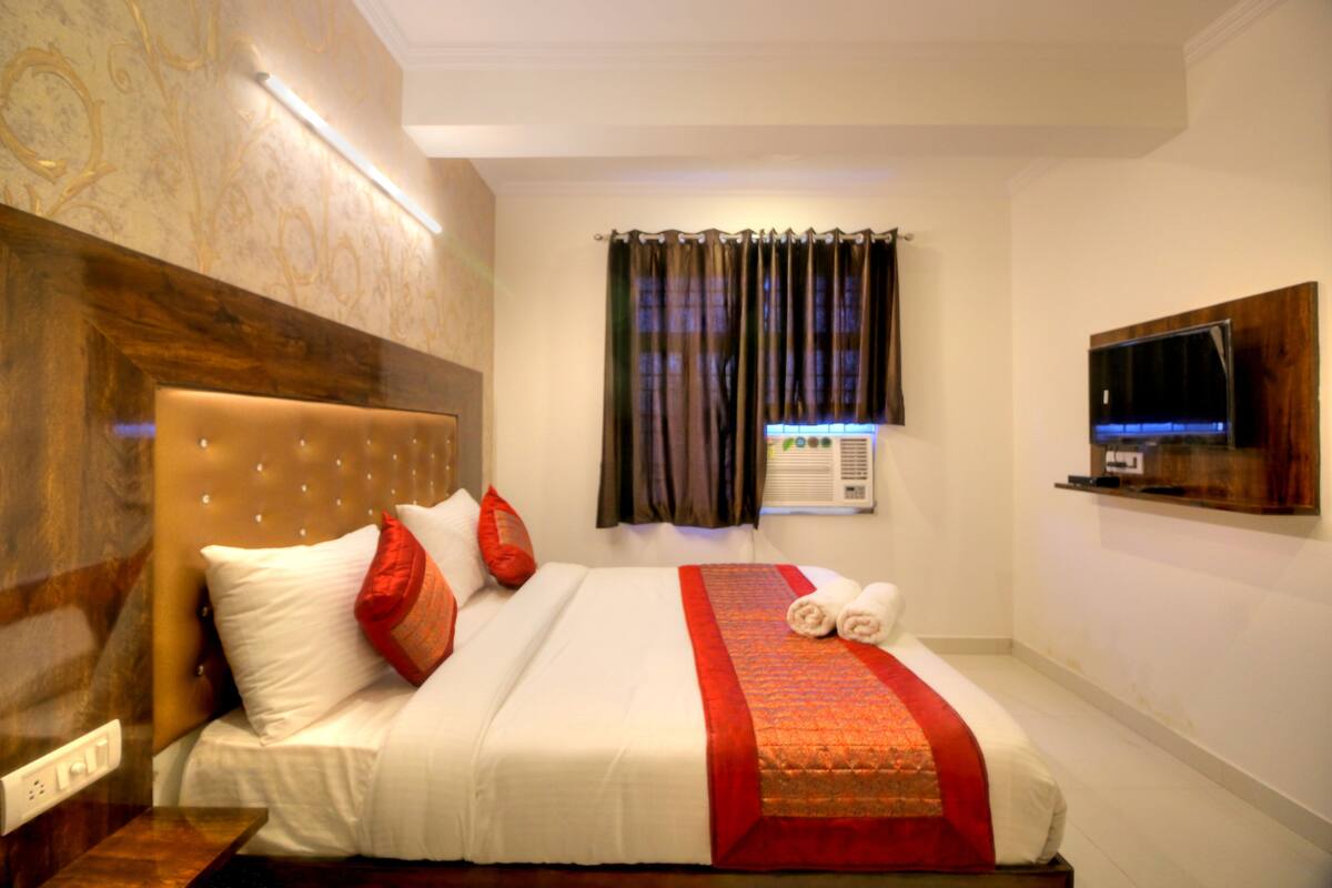 Habitación de hotel con una cama grande, televisión de pantalla plana, ventana con cortinas e aire acondicionado de pared.