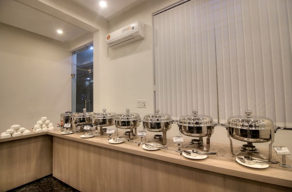 A buffet setup with multiple food service stations, a window, and an air conditioning unit on the wall.