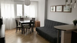 Un soggiorno moderno con parquet a spina di pesce, un divano grigio, un tavolo da pranzo con sedie e una lampada a sospensione.