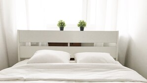 Un letto con una testiera bianca, due cuscini e una coperta bianca. Sulla testiera ci sono due piccole piante in vaso.