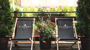 Two black lounge chairs with "SYKWONY" branding, positioned on a wooden deck with a potted plant between them. - Pensjonat Sykowny (Bialy Dunajec)