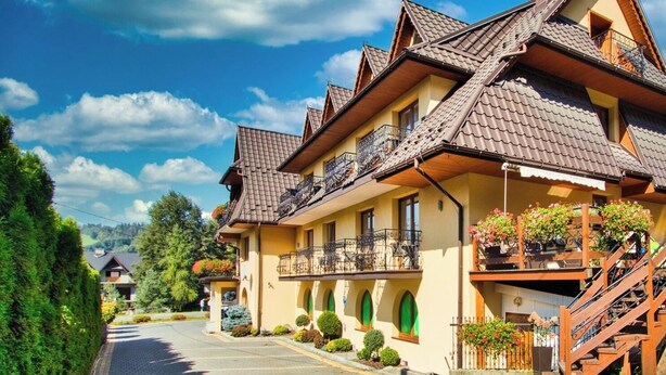 A row of traditional chalet-style buildings with balconies, a paved driveway, and surrounding greenery. - Pensjonat Sykowny (Bialy Dunajec)