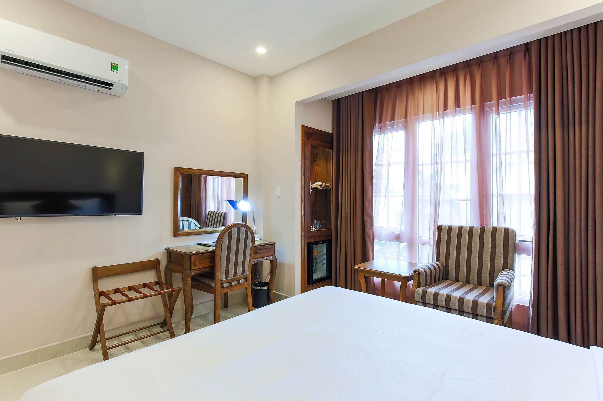 Una habitación de hotel con cama, escritorio con silla, televisor y ventana con cortinas.