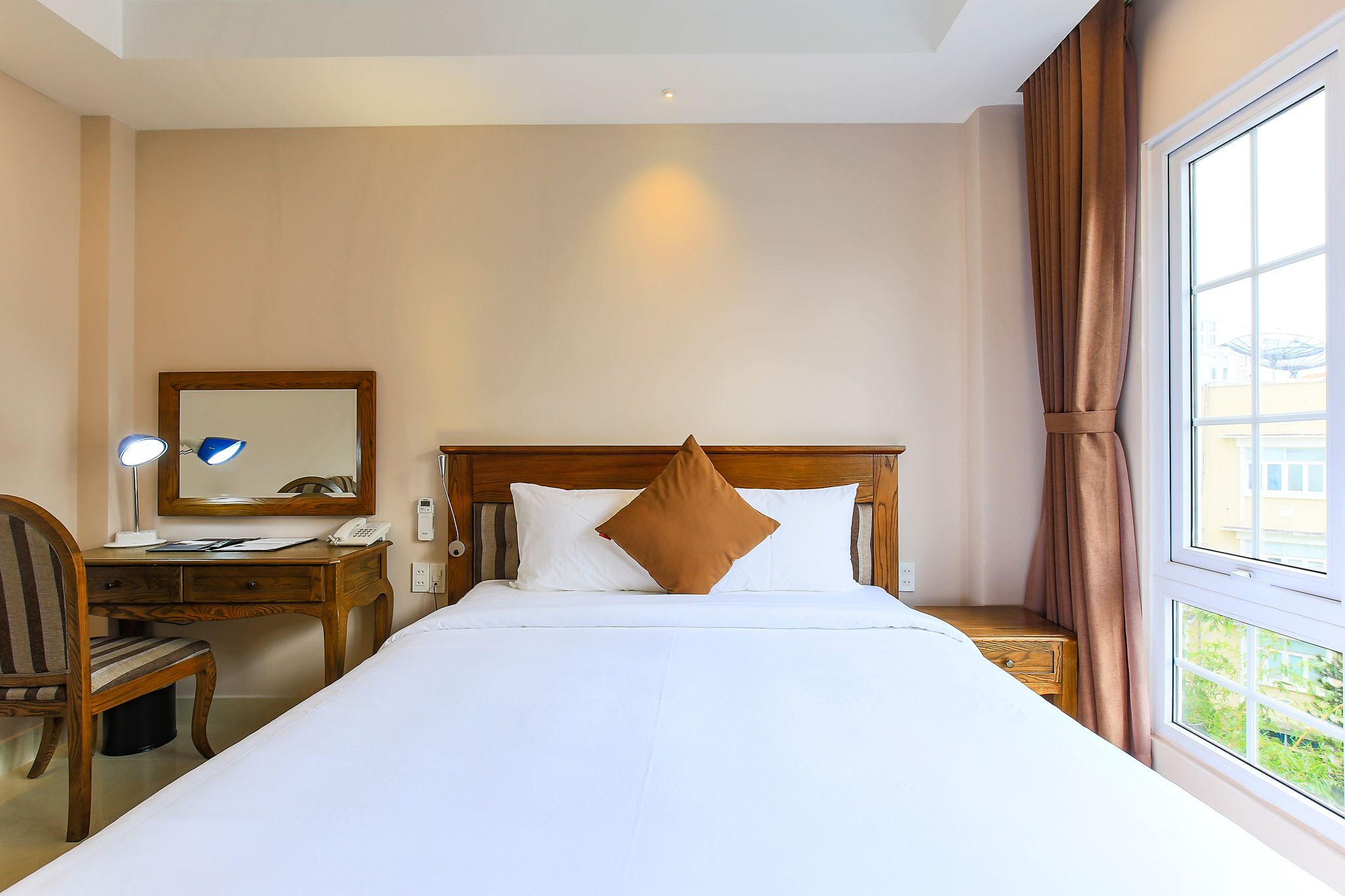 A hotel room with a bed, a desk, a chair, a mirror, and a window with curtains.
