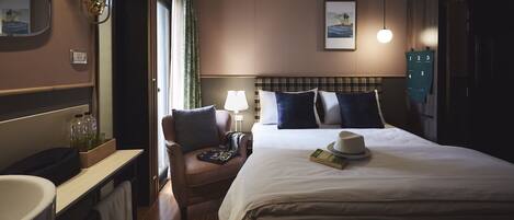 A hotel room with a large bed, a chair, a desk, a lamp, and a wall-mounted clock.