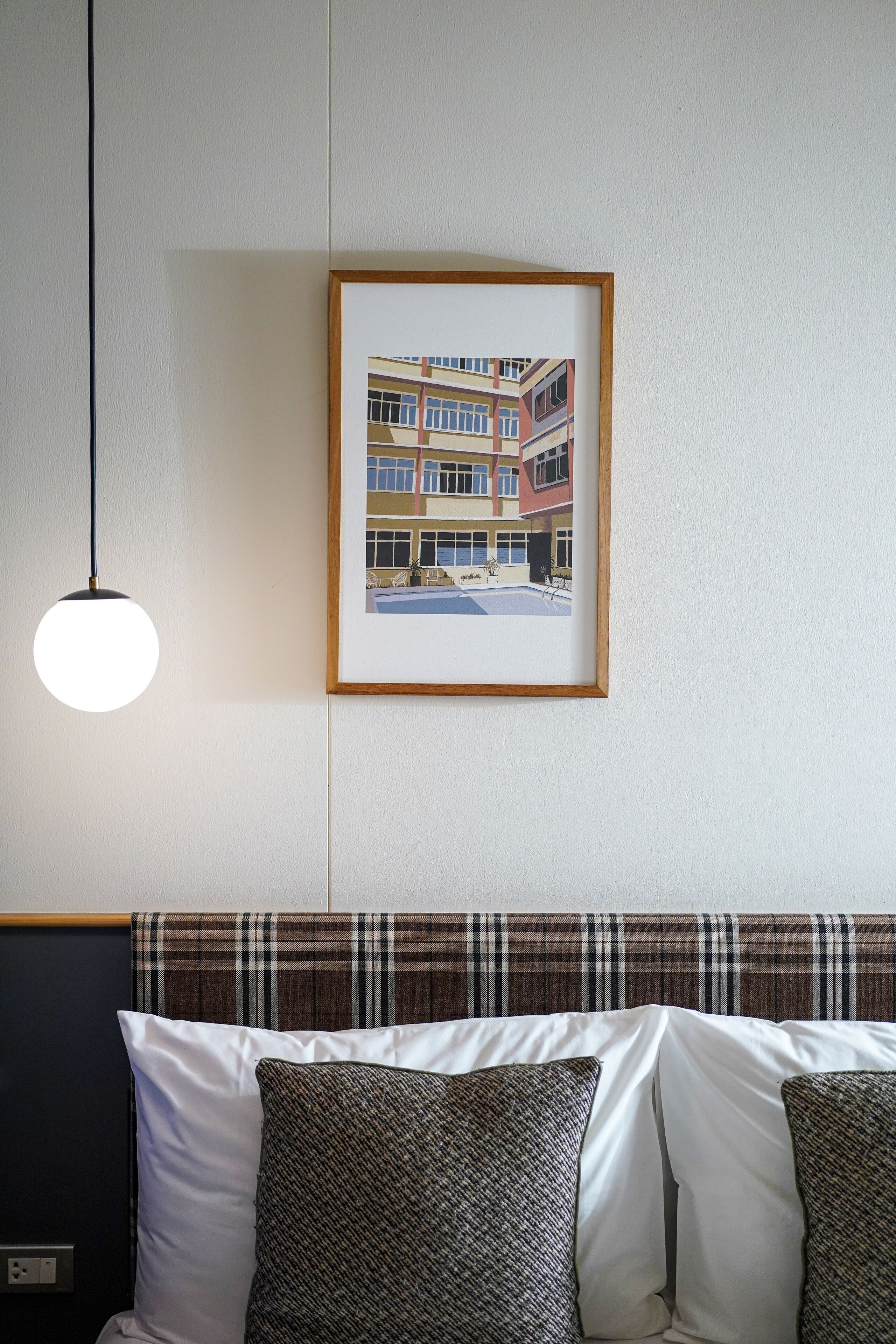 A framed artwork of a building on a wall, a hanging light fixture, and a sofa with patterned cushions.
