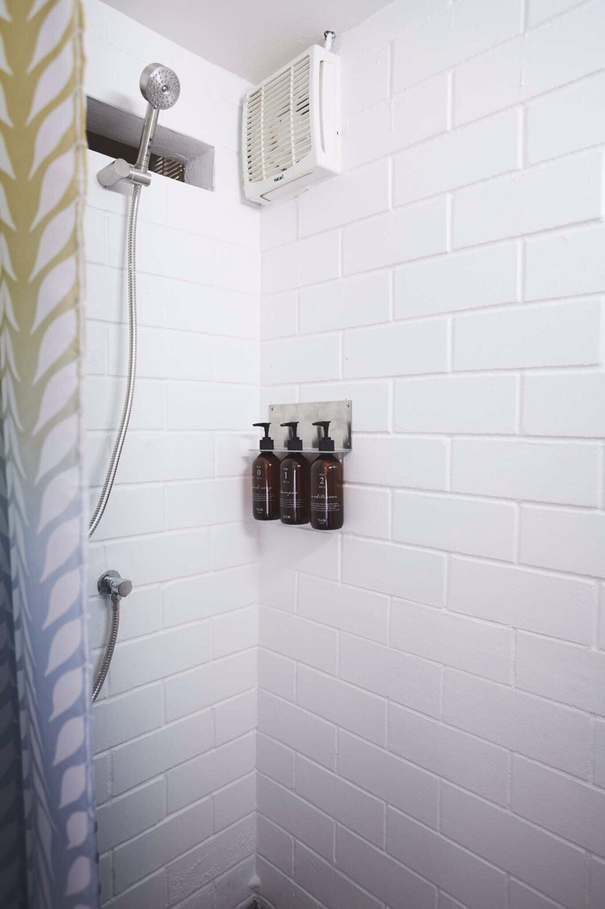 Une douche équipée d’un pommeau de douche à main, d’un radiateur mural et d’un distributeur de savon.