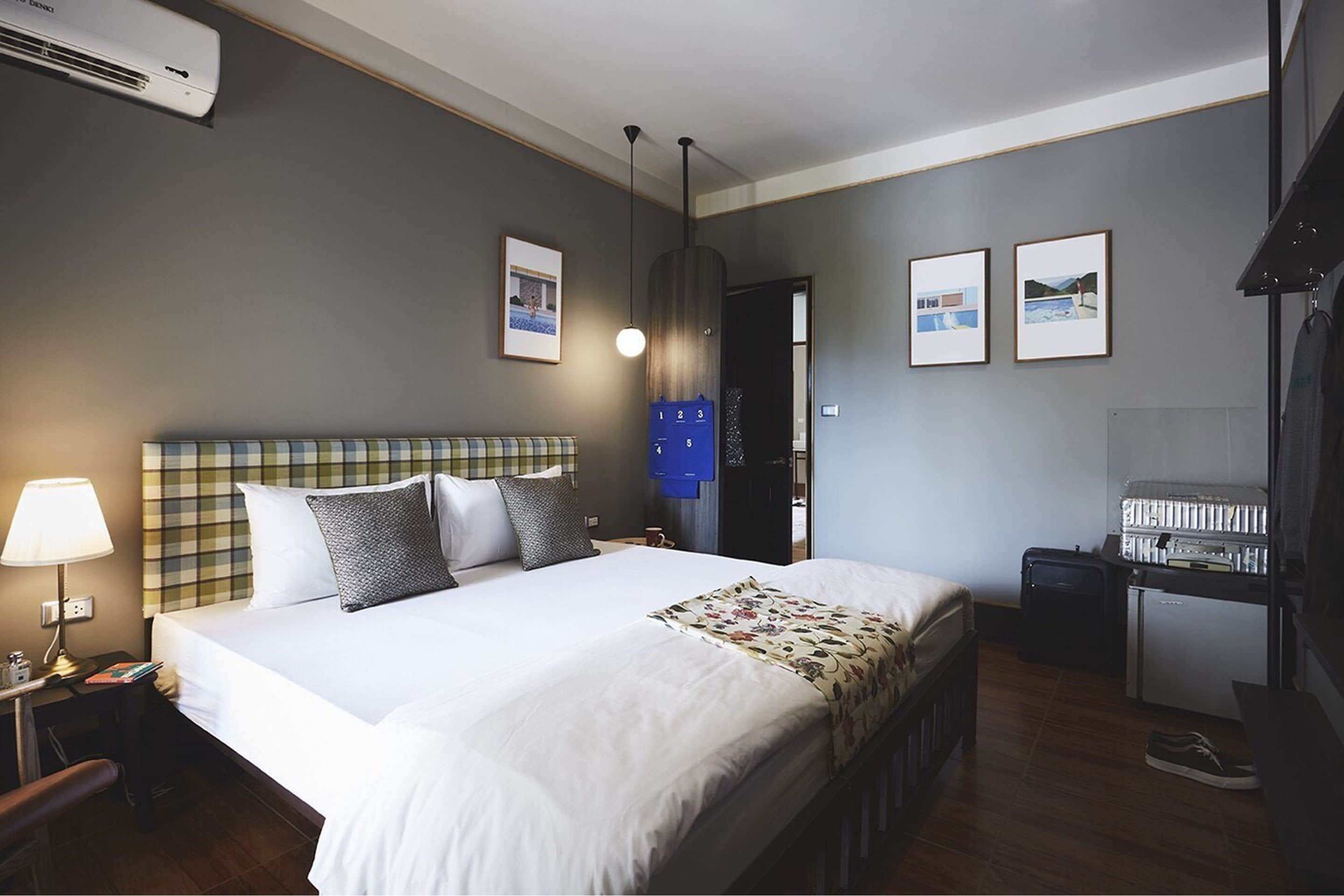 Habitación de hotel con cama, escritorio, silla, lámpara y aire acondicionado instalado en la pared.