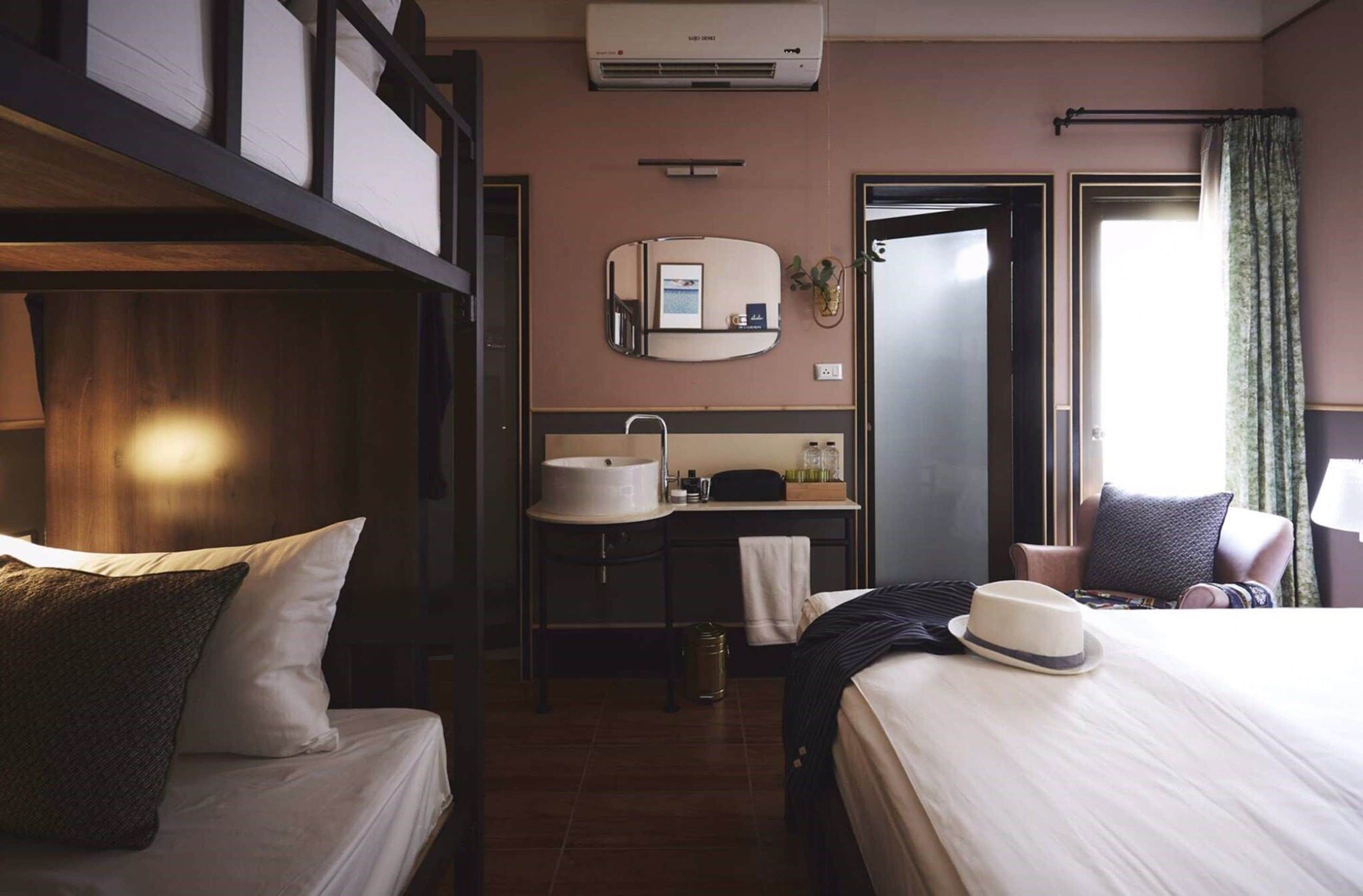 A hotel room with bunk beds, a small desk with a sink, a mirror, and a window with curtains.