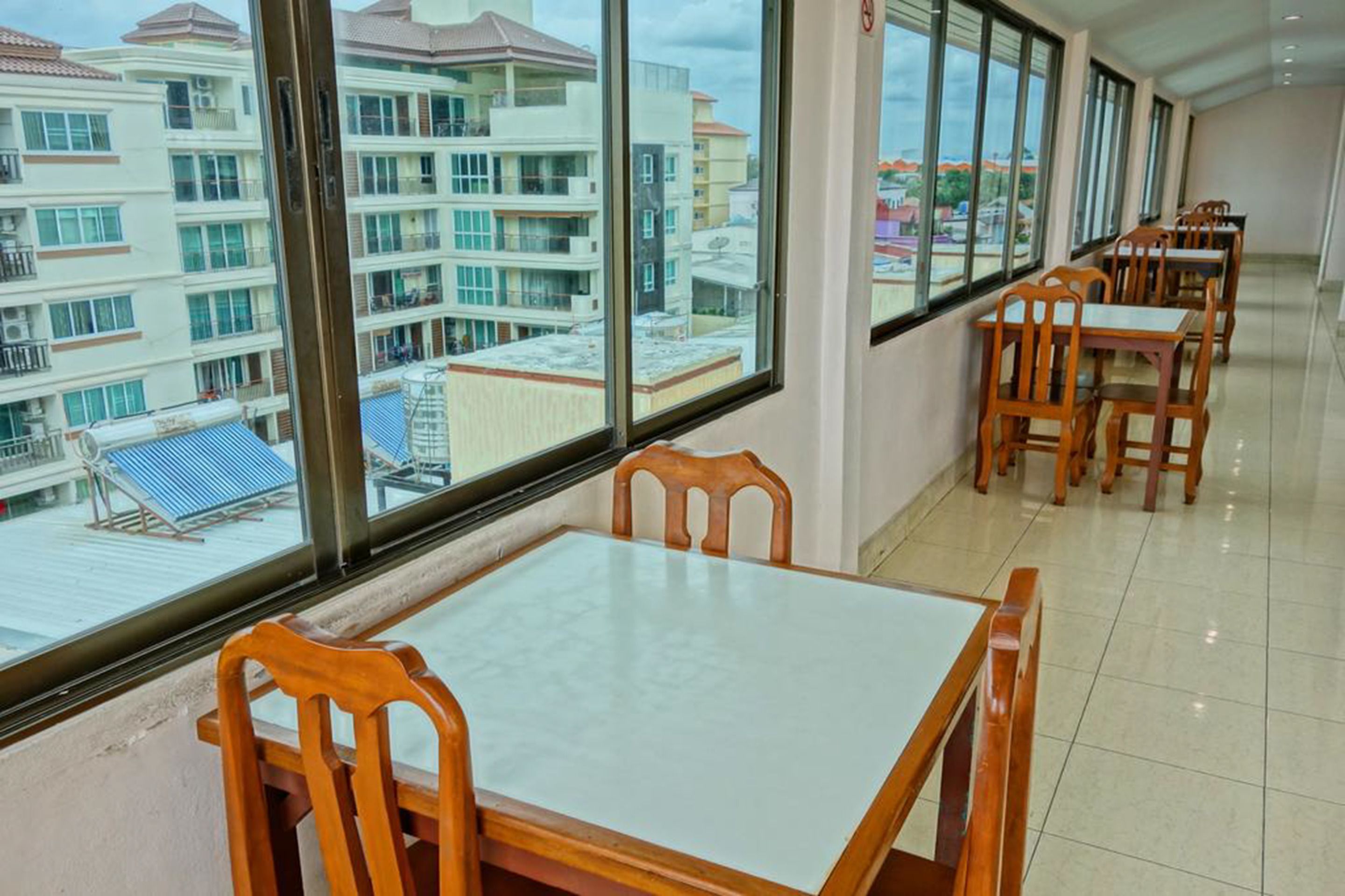 A hotel dining area with wooden tables and chairs, large windows offering views of buildings and a blue-roofed structure outside.