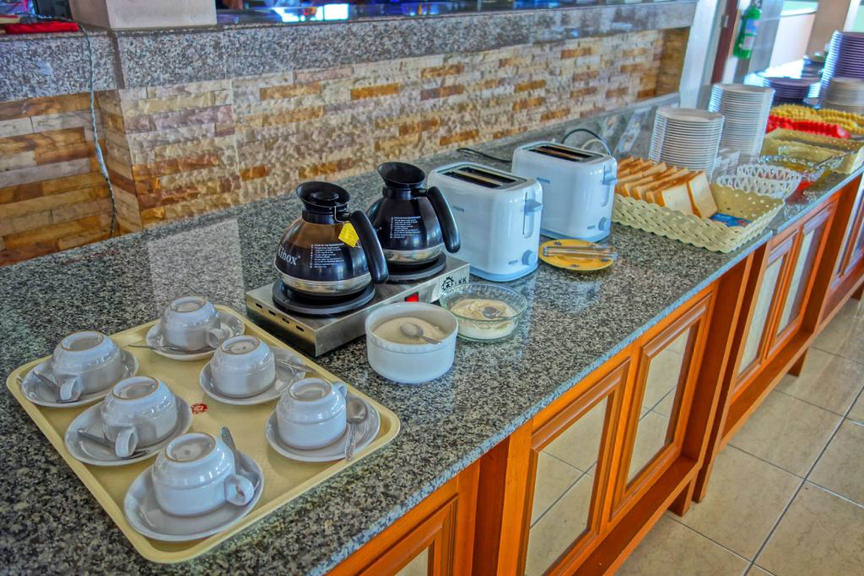 A buffet setup with coffee makers, toasters, and various food items on a granite countertop.