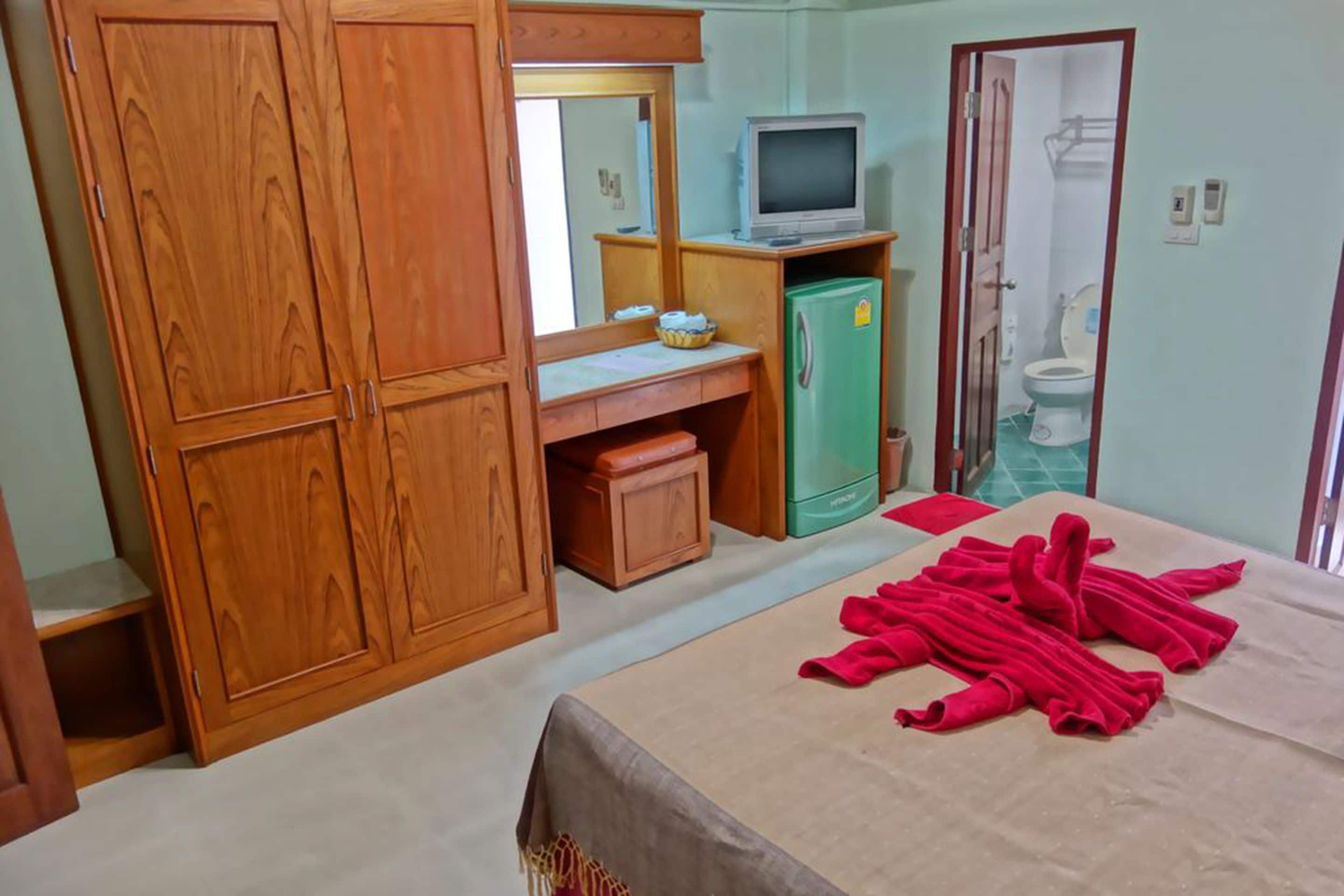 A bedroom with wooden cabinets, a television, a green refrigerator, and a bed with red towels.
