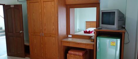 A room with a wooden wardrobe, a desk with a mirror, a green Hitachi refrigerator, and a television on a wooden stand.