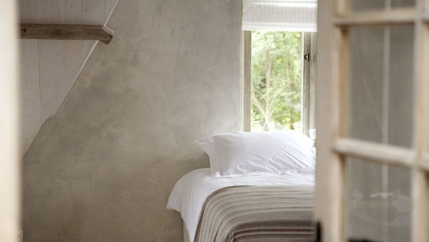 Quarto com cama, janela e vista para o verde lá fora.