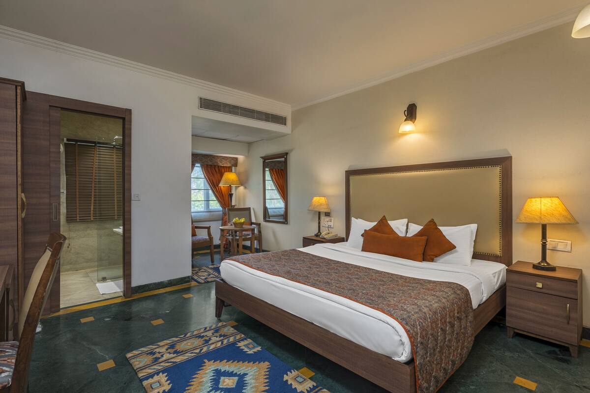 A hotel room with a large bed, a desk, a chair, a small table, and a mirror.