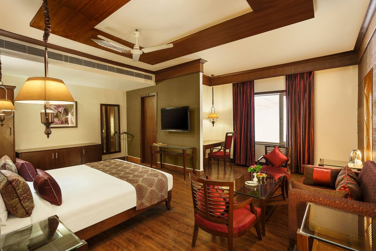 A hotel room with a large bed, a desk, a chair, a sofa, a TV, and a window with curtains.