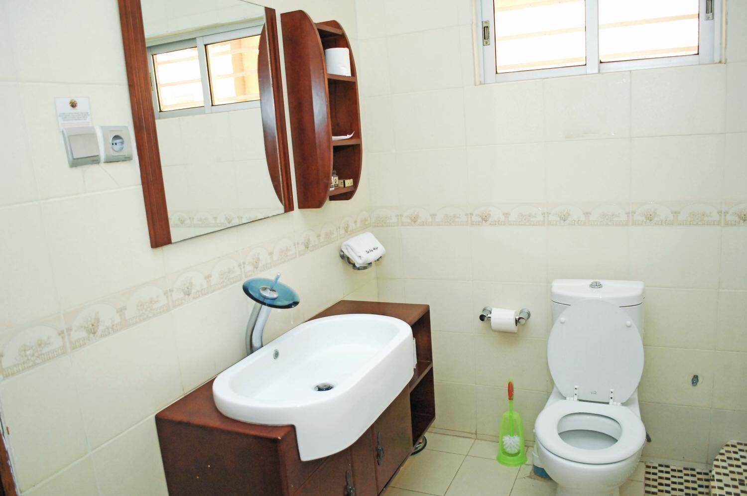 A bathroom with a sink, mirror, toilet, and a window.