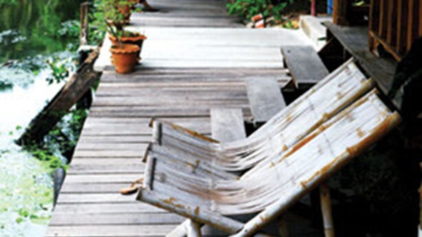 A wooden deck with lounge chairs, a thatched roof, and potted plants. - Baan Suanaomsuk (Pak Tho)