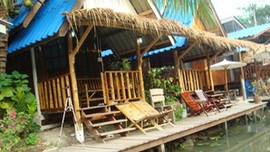 A wooden dock with lounge chairs and umbrellas, leading to a building with a thatched roof and blue walls. - Baan Suanaomsuk (Pak Tho)