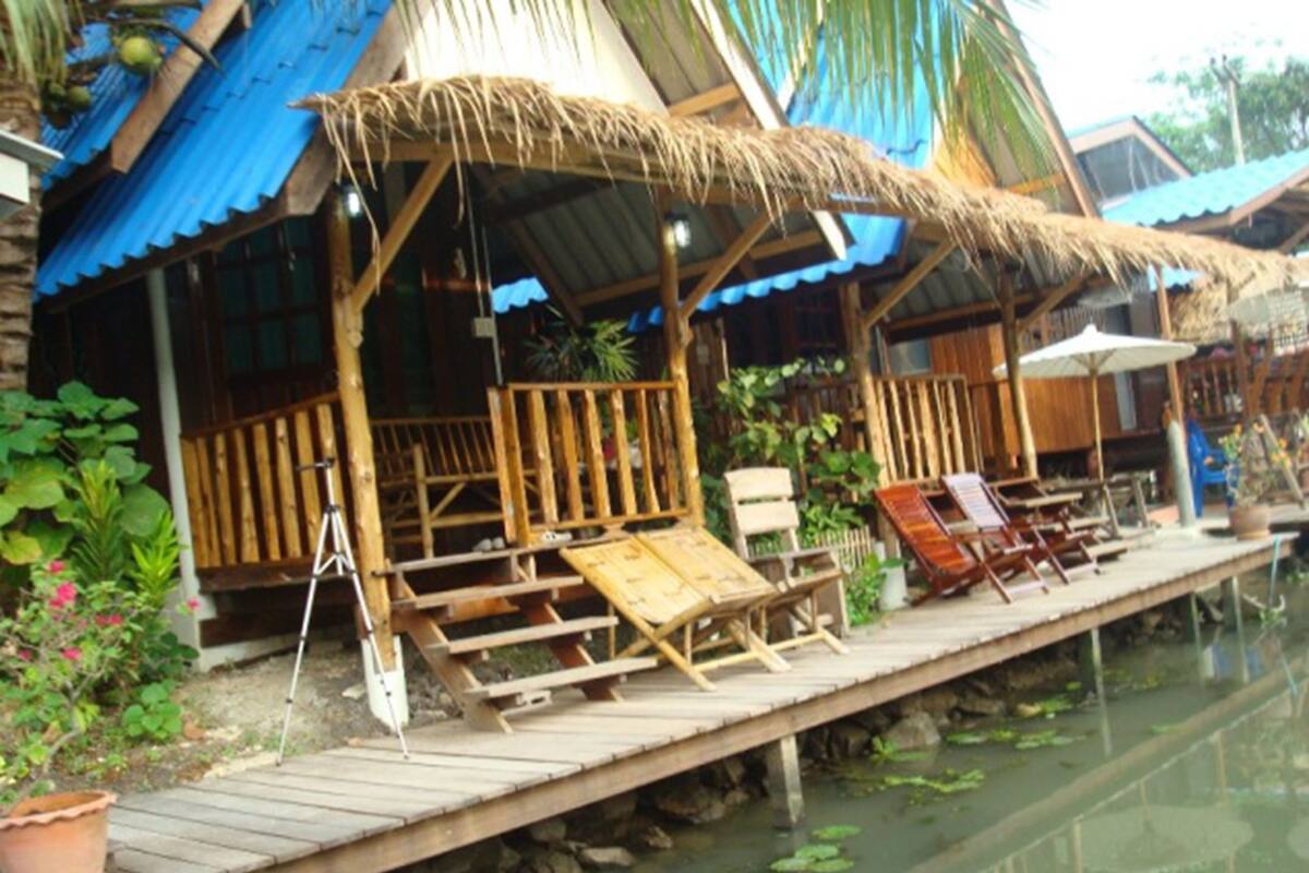 A wooden dock with lounge chairs and umbrellas, leading to a building with a thatched roof and blue walls.