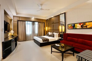 A hotel room with a bed, a red sofa, a TV, a desk, and a ceiling fan.