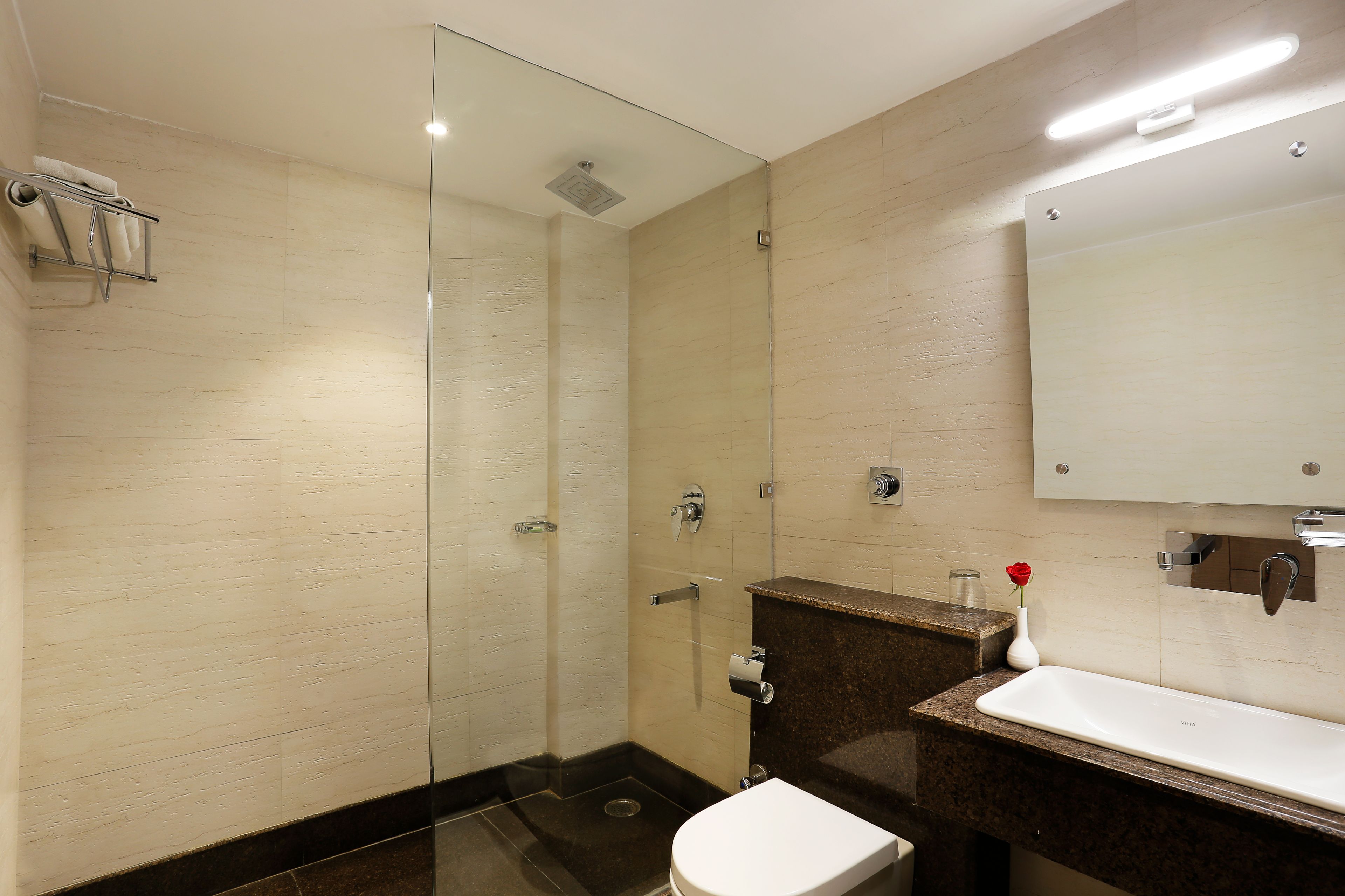 Un baño moderno con cabina de ducha de vidrio, inodoro blanco, lavabo de mármol y un espejo sobre el lavabo.
