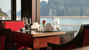 Mesa de jantar posta para dois, com vista para um corpo de água e montanhas ao fundo.