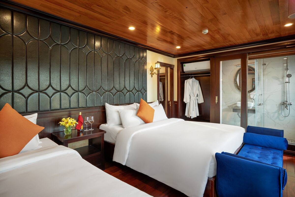 A hotel room with two beds, a wooden ceiling, a glass shower area, and a small seating area.