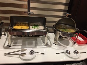 A buffet setup with two serving stations, one with a yellow dish and another with a green dish, and a red basket on the right. - Lan Ha Legend Cruise (Bai Chay)