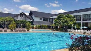 Una piscina con sillones de descanso y sombrillas, rodeada de edificios de estilo arquitectónico moderno.