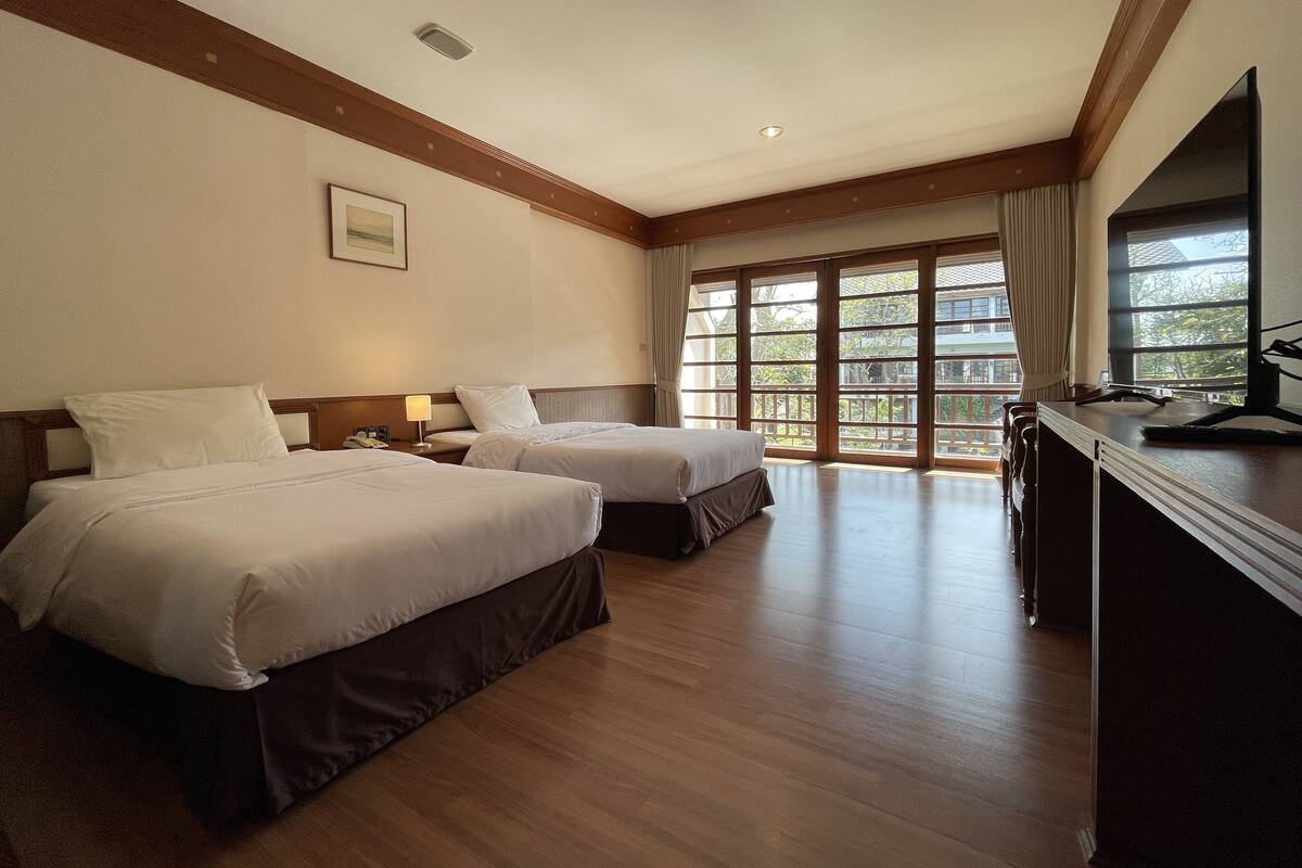 Una habitación de hotel con dos camas, un escritorio y ventanas grandes.