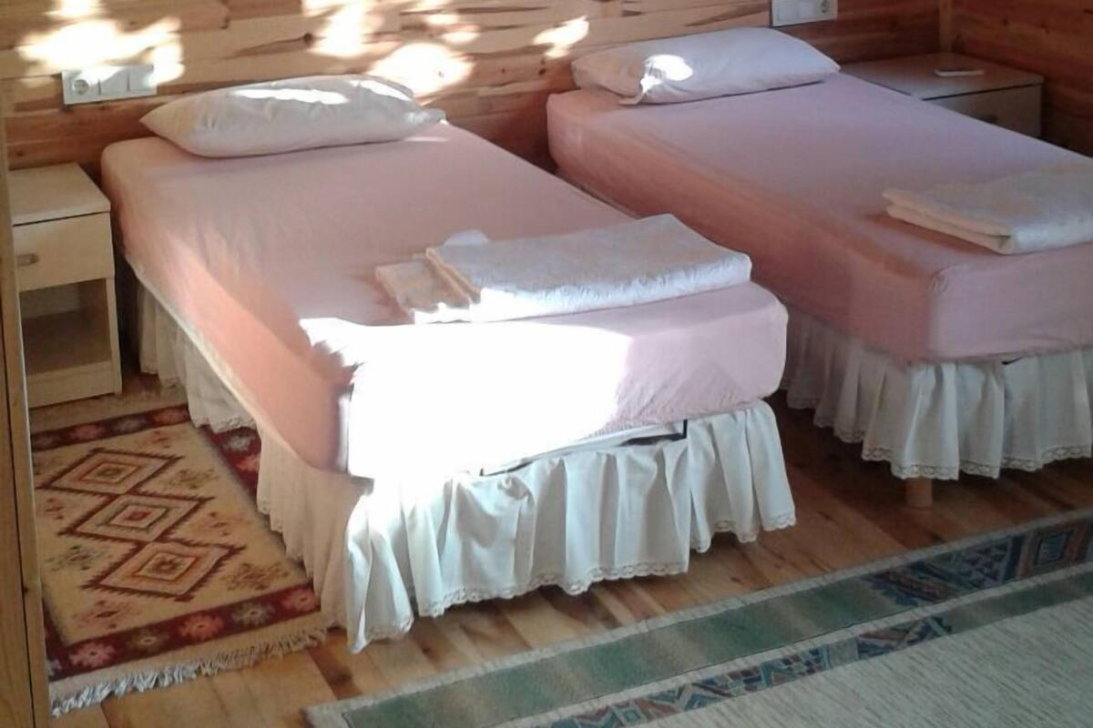 A wooden cabin room with two beds, a small table, and an air conditioning unit.