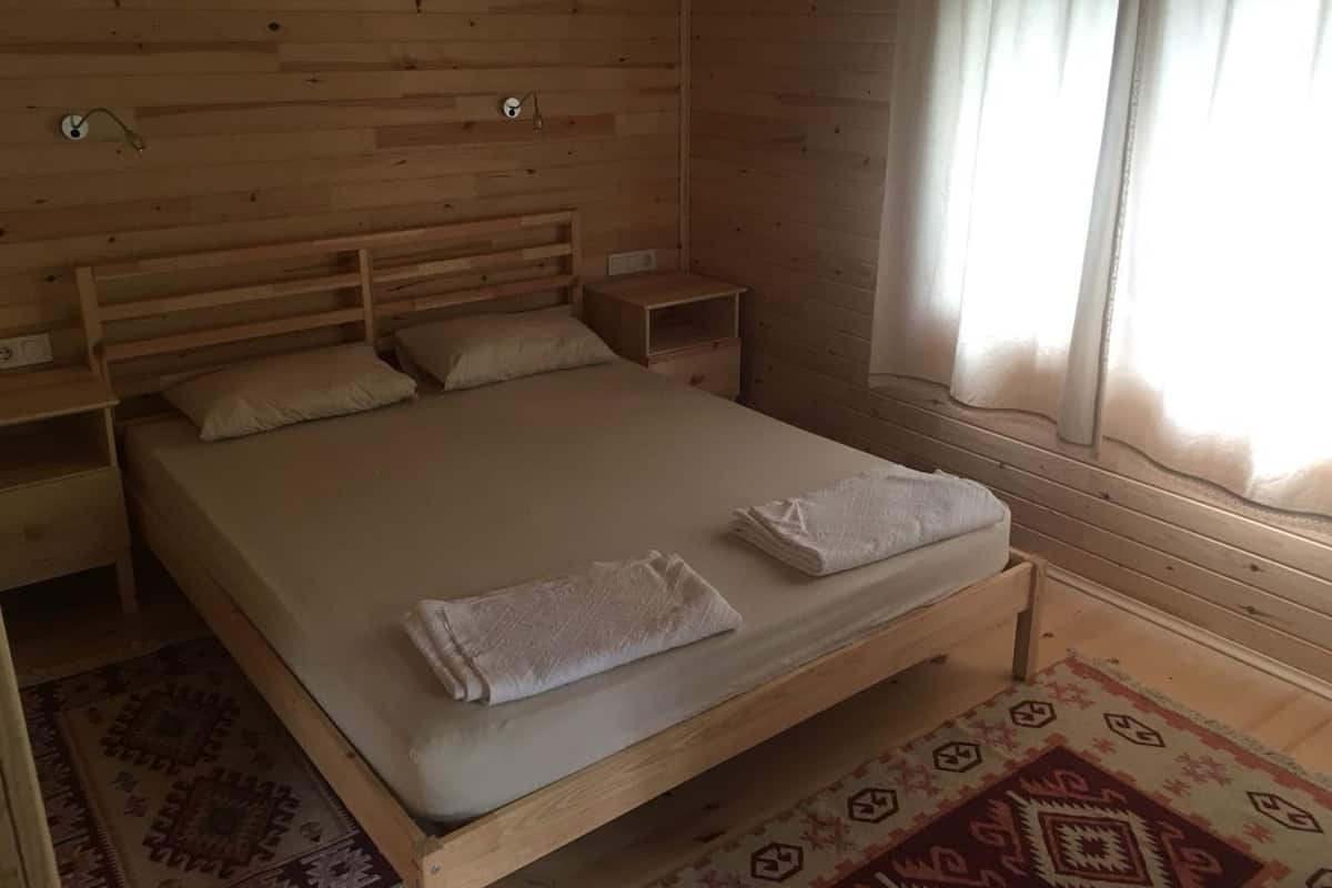 A wooden room with a bed, nightstands, and a window with curtains.