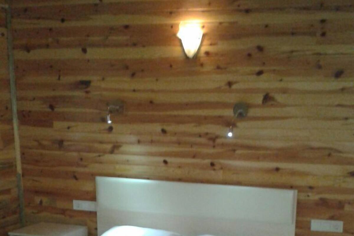A wooden-paneled room with a bed, two bedside tables, and a wall-mounted light fixture.