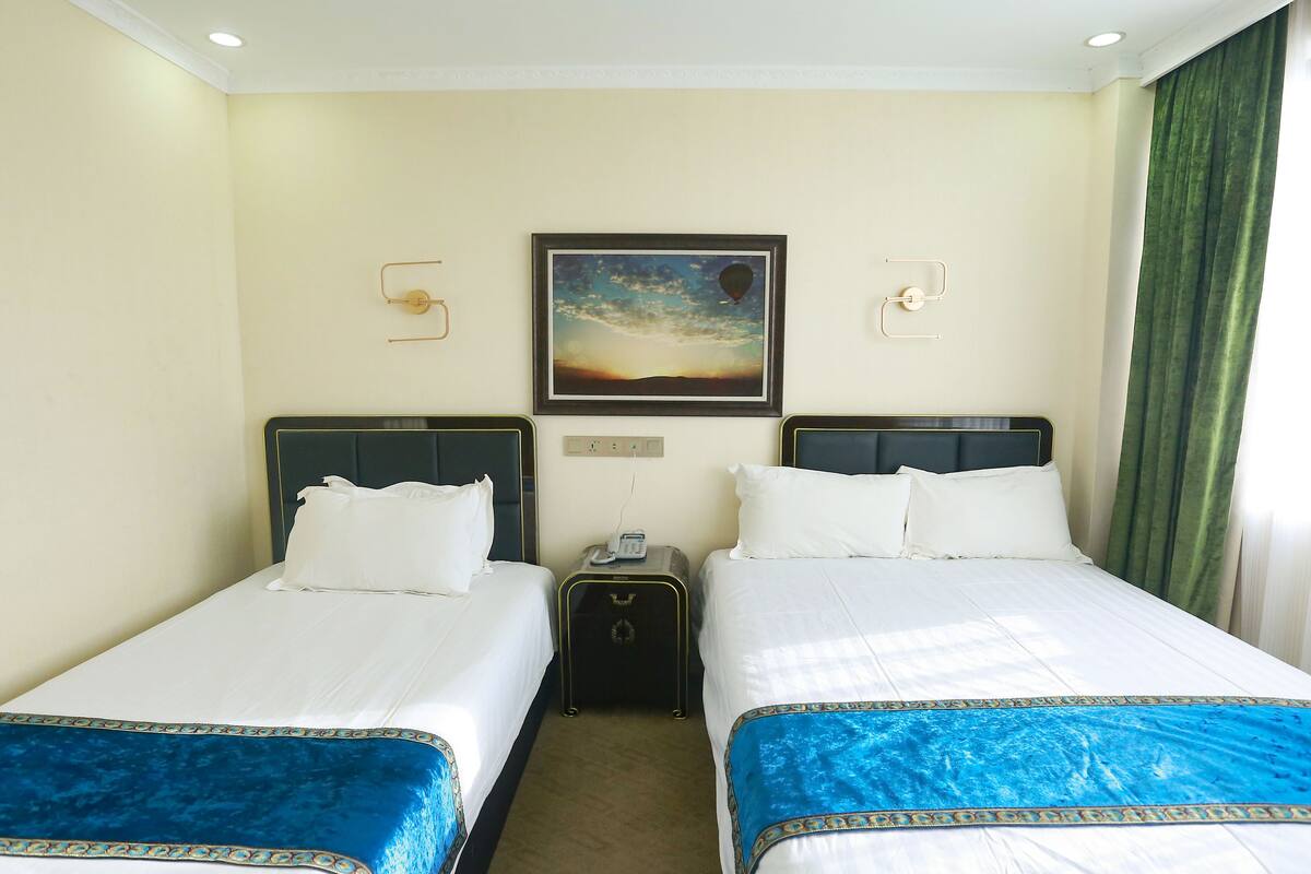 A hotel room with two beds, a painting of a hot air balloon, a telephone on the nightstand, and a green curtain.