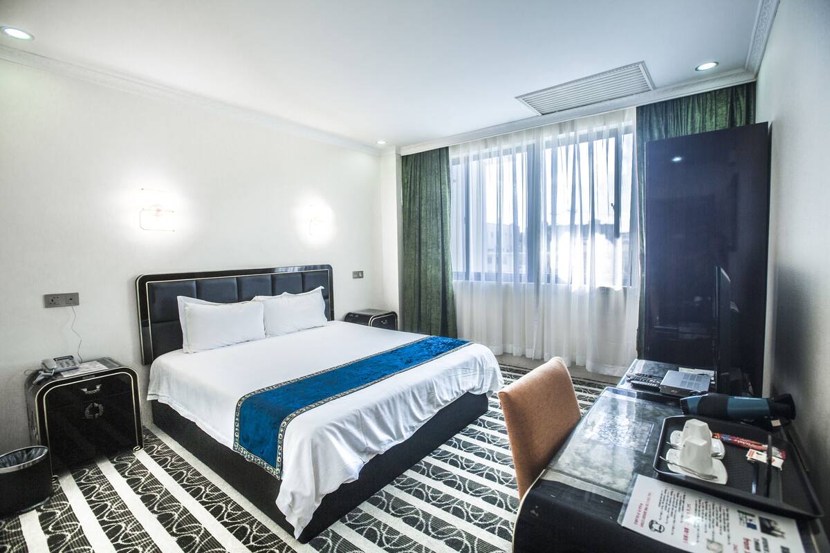 A hotel room with a bed, bedside table, desk, chair, and a television.