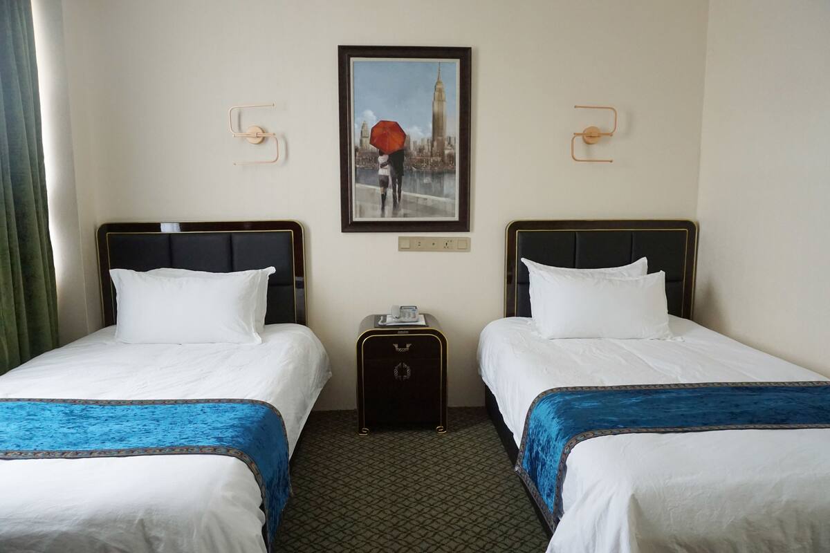 A hotel room with two beds, a small table with a phone, and a framed picture on the wall.