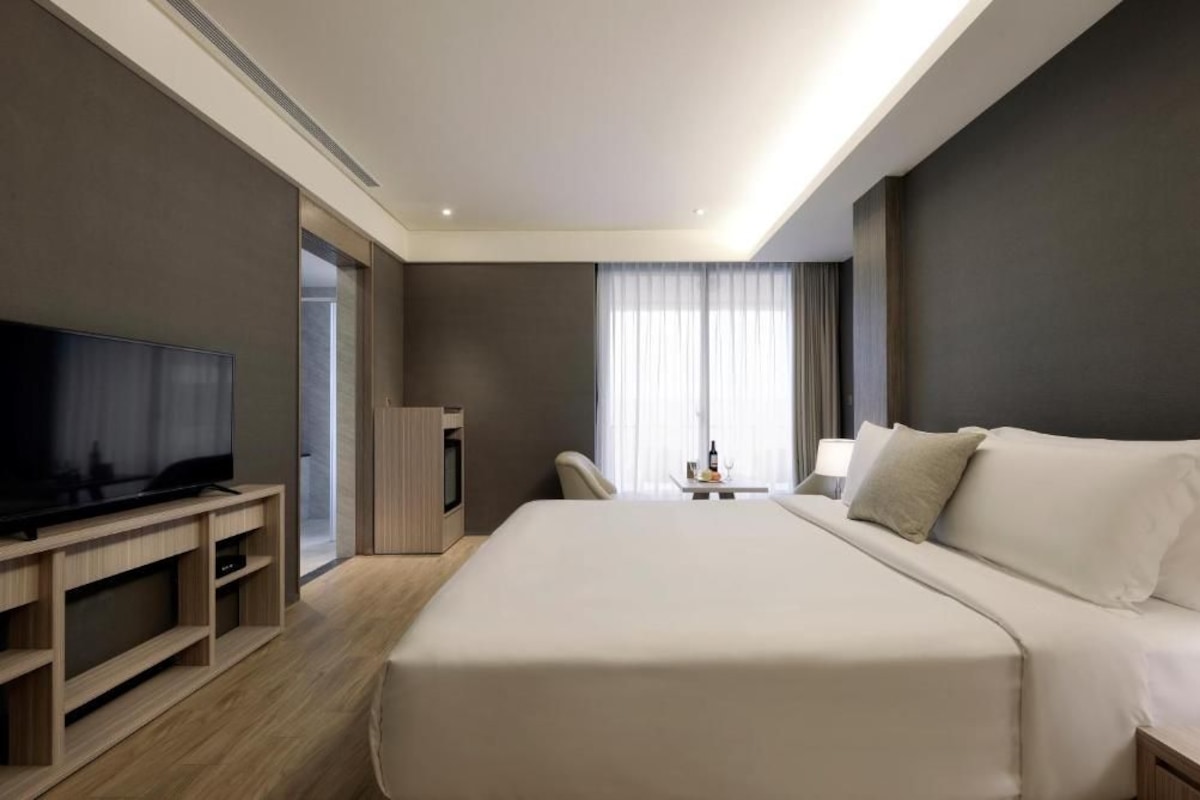 A hotel room with a large bed, a television on a wooden stand, a desk with a lamp, and a window with curtains.