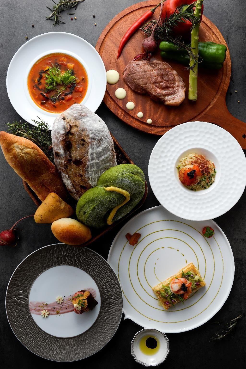 Variedad de platos que incluyen sopa, filete y un aperitivo de mariscos, dispuestos en diferentes fuentes y una tabla de madera.