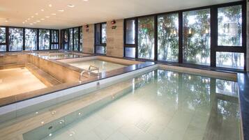 En stor indendørs swimmingpool med flere baner, omgivet af store vinduer med udsigt til træer.