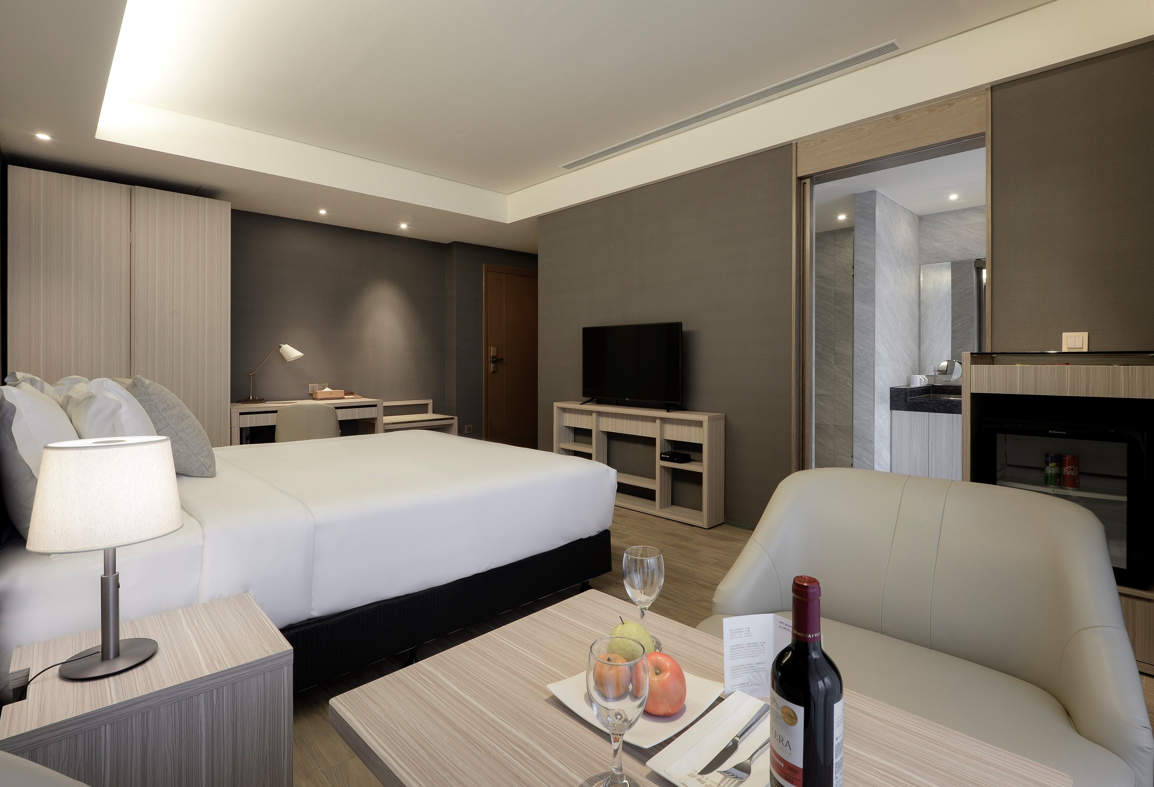 A hotel room with a bed, a desk, a television, a minibar, and a seating area.