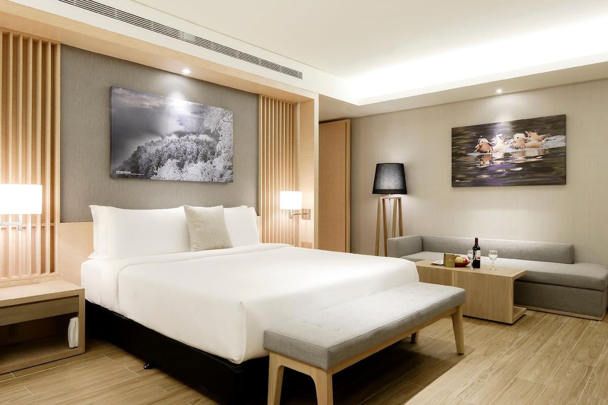 Una habitación de hotel moderna con una cama grande, un sofá, una mesita con una lámpara y dos lámparas de pared.