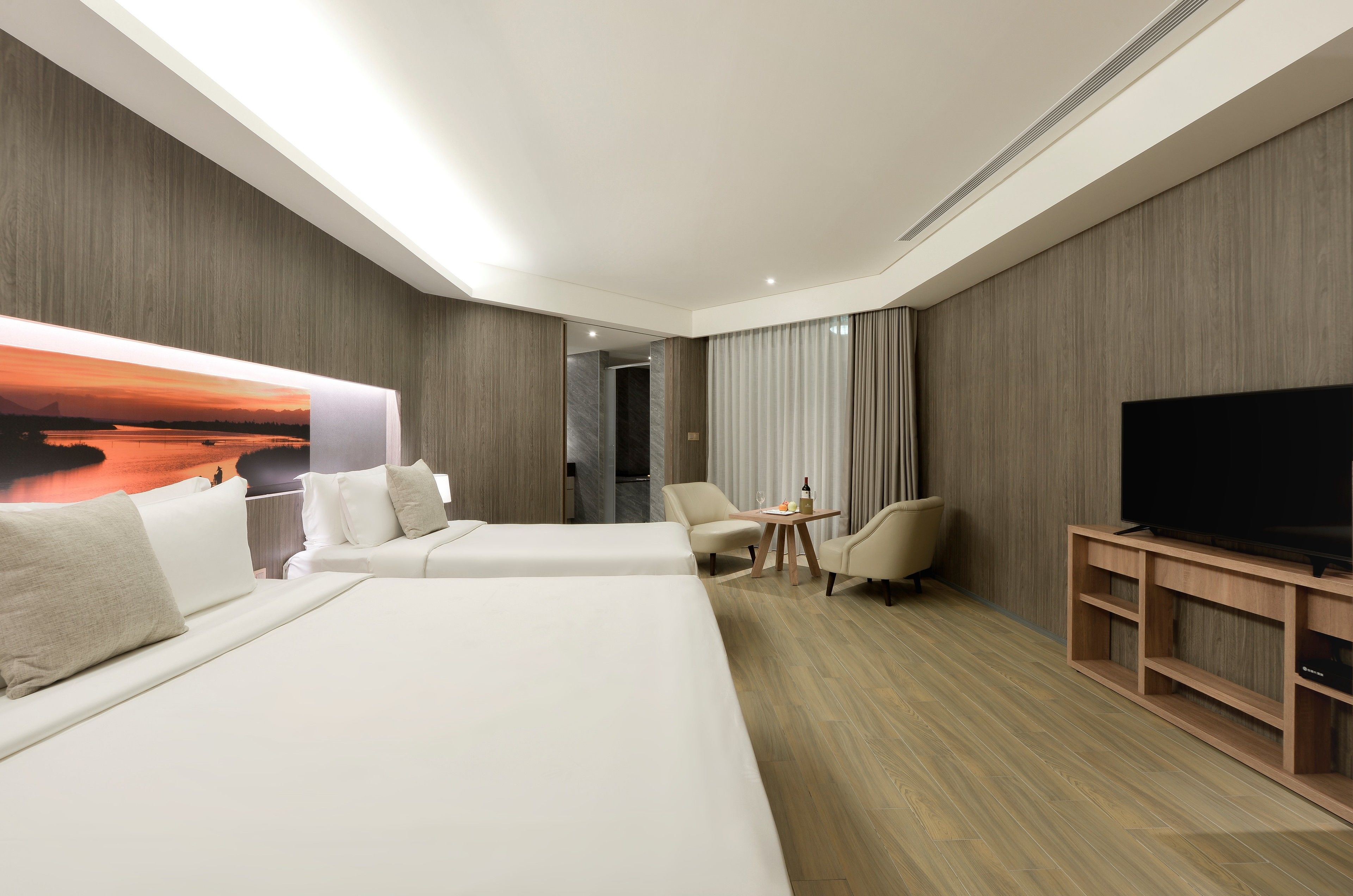 A hotel room with two beds, a TV, a small table with a bottle, and a chair.