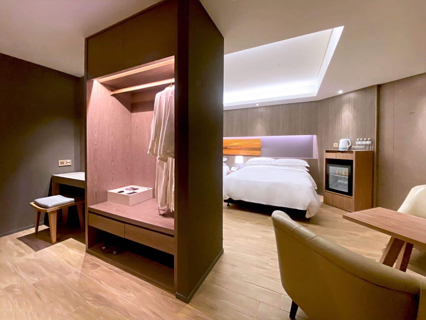 Quarto de hotel moderno com cama, escrivaninha, cadeira, mesinha e armário embutido.