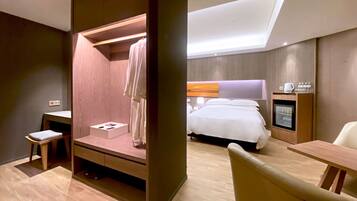 Quarto de hotel moderno com cama, escrivaninha, cadeira, mesinha e armário embutido.