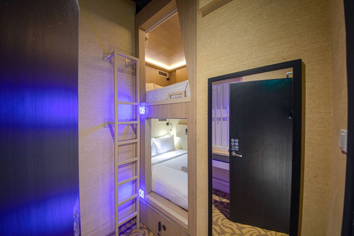 A compact hotel room with a bunk bed, a small desk, and a door with a keypad lock.